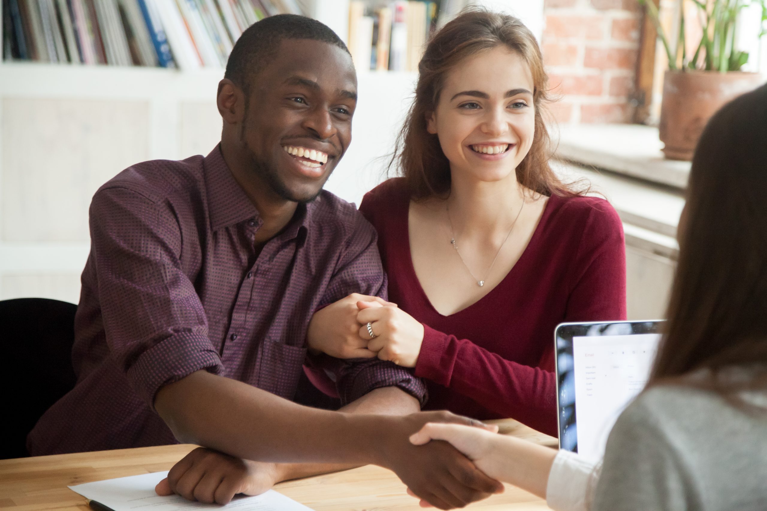 A happy young couple learn that they are eligible for a debt consolidation loan and shake the provider's hand in agreement